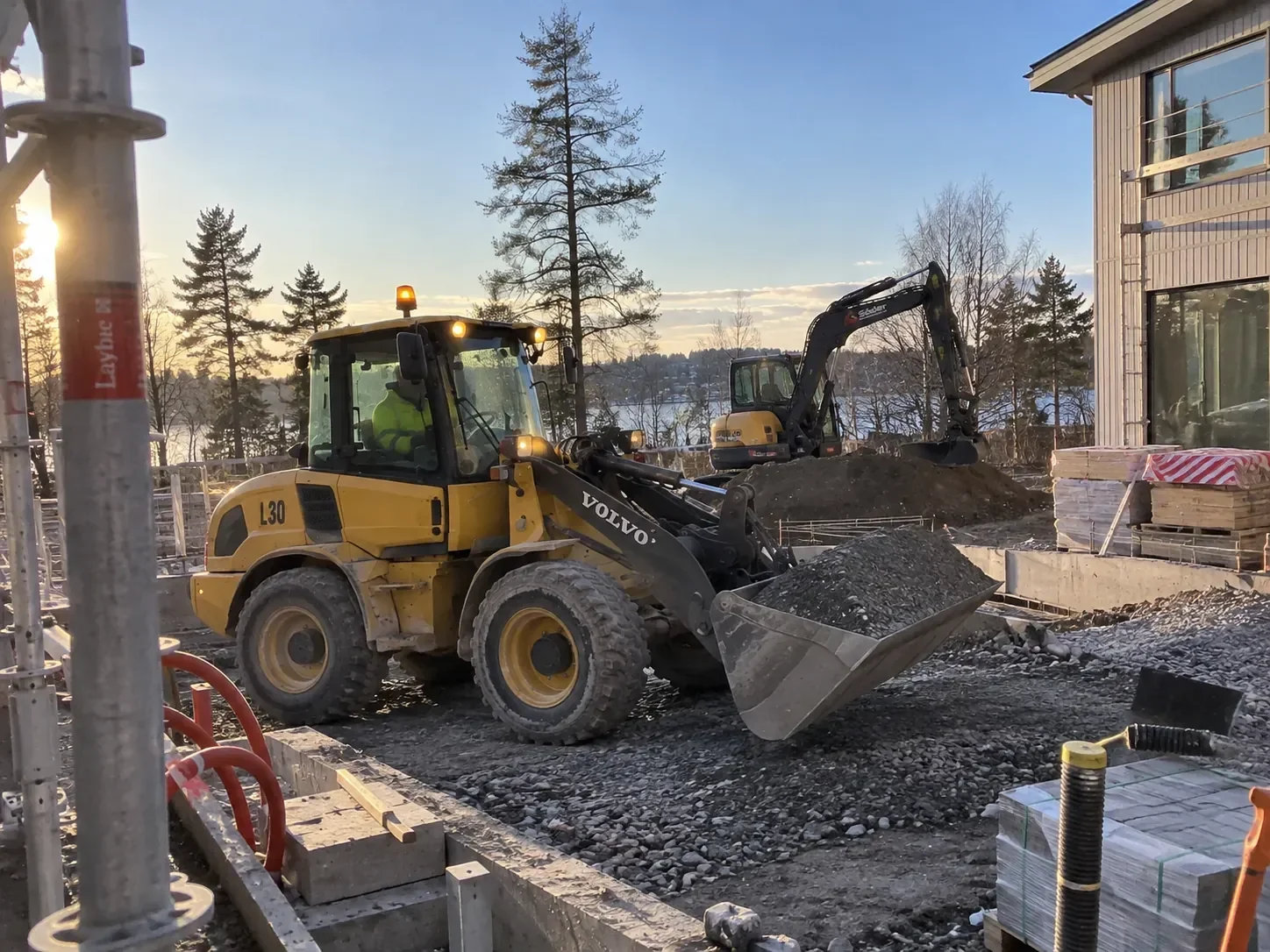 Volvo L30 lastar makadam på en byggarbetsplats med grävmaskin i bakgrunden